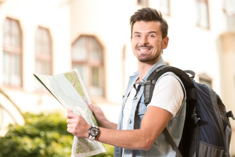 Trendy young man in the town with touristic map and backpack.