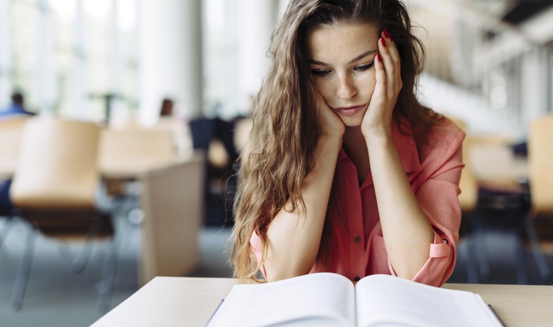 Female student studying and reading in a library but is having a hard time understanding the material