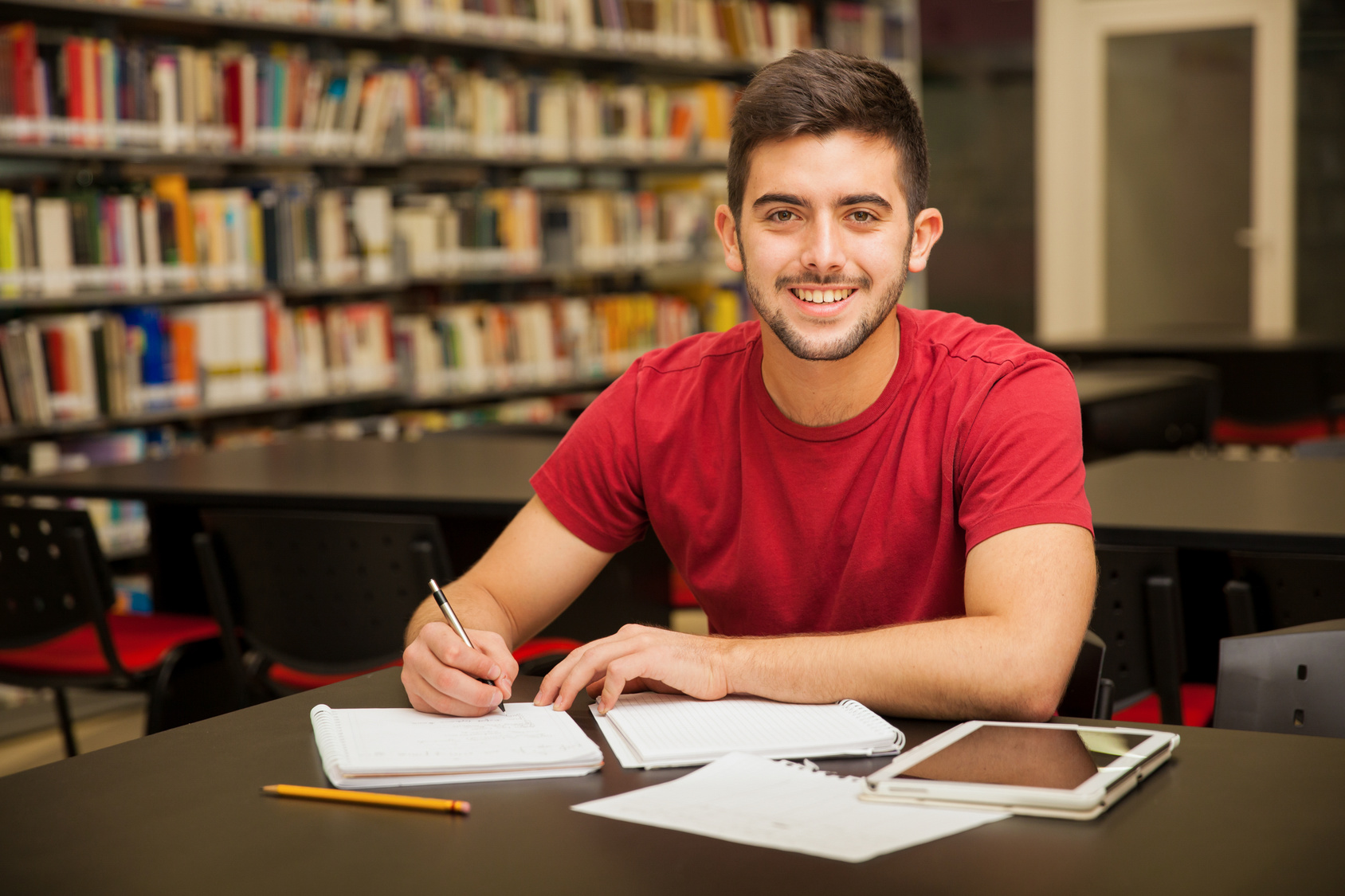 Attractive male university student doing some homework in the school library and smiling